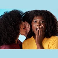 2 black women gossiping. woman whispering in shocked friend's ear. turquoise background.