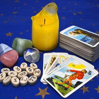 divination psychic items, tarot cards, gemstones, crystals, runes, partially burned down unlit yellow candle, all on a blue table with gold stars