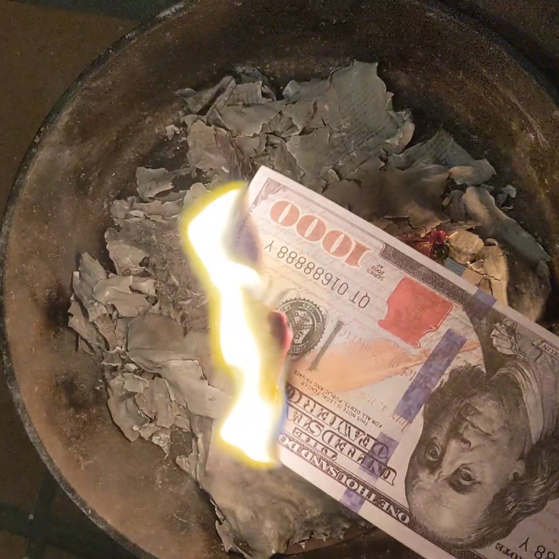a joss paper note with a burning corner edge over a pot of ashes 