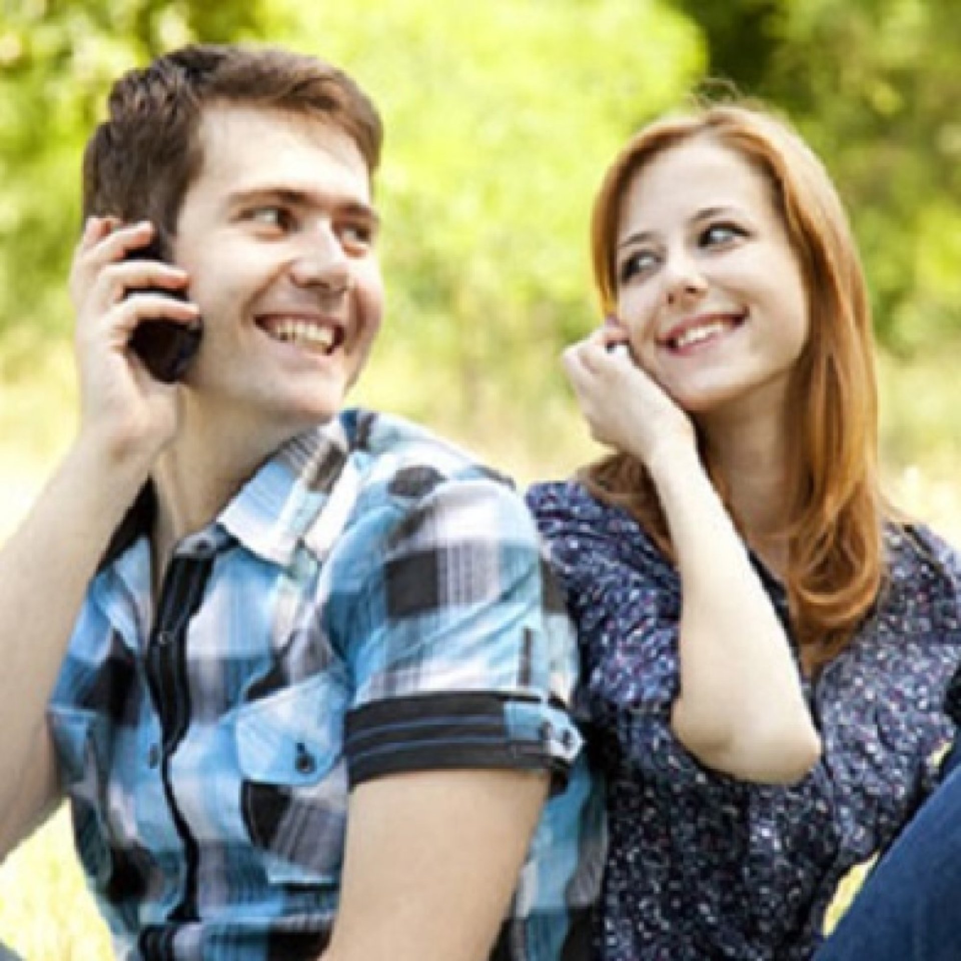man woman couple sitting back to back, looking over their shoulders and smiling at each other while, holding phones