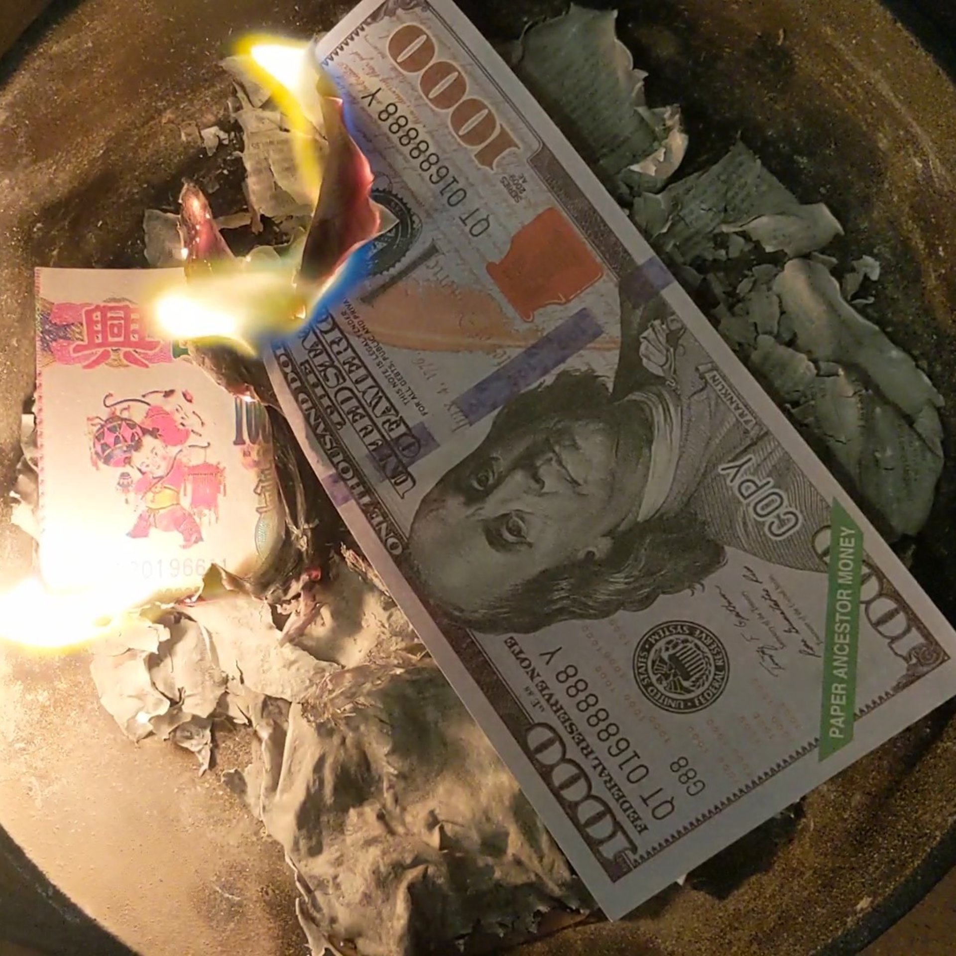 two joss paper notes burning in a pot of ashes 